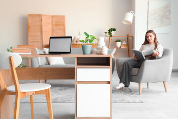 Blank laptop with plant and books on female programmer's desk in living room