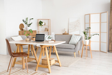 Interior of light living room with programmer's workplace, sofa and armchair