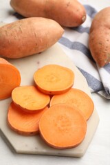 Fresh sweet potatoes and kitchen towel on white table, closeup