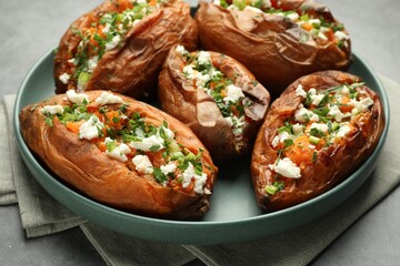Tasty cooked sweet potatoes with feta cheese, green onion and parsley on gray table, closeup
