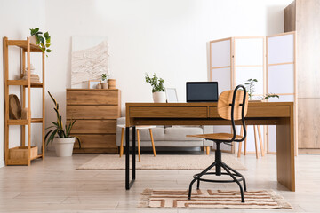 Interior of light living room with programmer's workplace, folding screen and plants