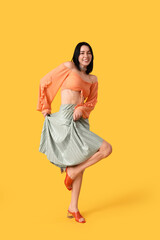 Naklejka premium Happy young woman in skirt dancing on yellow background