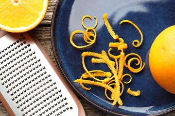Fresh orange zest, fruits and grater on wooden table, flat lay