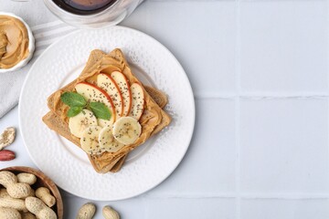 Tasty sandwich with peanut butter, apple, banana, chia seeds, nuts and mint on white tiled table, flat lay. Space for text