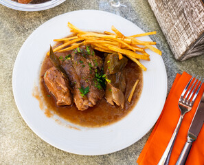 On round white plate are pieces of stewed beef veal meat tenderloin fillet, garnished with French fries. Glass of dry red wine and slices of white bread are served for lunch