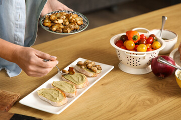 Young woman with mushrooms cooking vegan bruschettas at table in kitchen, closeup