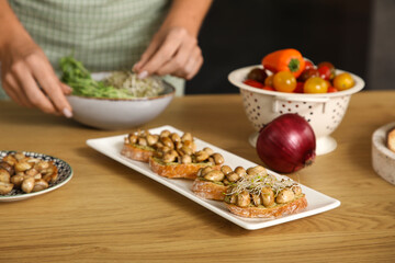 Tasty vegan bruschettas on table against woman cooking in kitchen, closeup