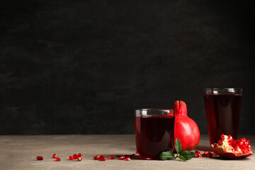 Glasses of fresh pomegranate juice and seeds on white table near black wall
