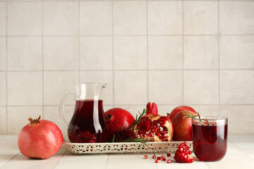 Glass and jug of fresh pomegranate juice with rosemary on white tile background