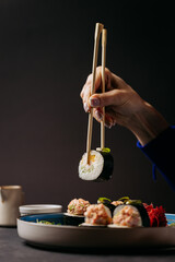 Hand holding sushi roll with chopsticks, showcasing fresh ingredients of cucumber and crab