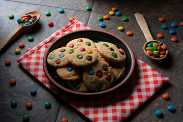 Group of red, blue, green and yellow vanilla chocolate chip cookies on a round black plate on a red napkin with white checks