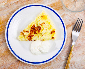 Delicious and dietary homemade food, piece of cottage cheese casserole is on plate. Dish is complemented with sour cream. Top view, breakfast served.