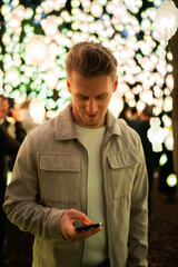 a man stands among beautiful colored lights in the dark and looking at the phone at Ekebergparken Oslo