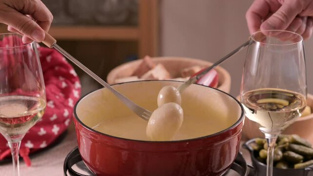 Cozy Swiss fondue setup with melted cheese, bread, pickles, and wine on a rustic table. advertising, social media campaigns, or food-related promotions. High quality 4k footage