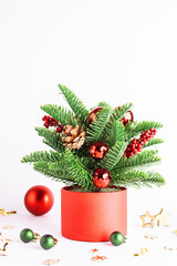 Bright Christmas composition made with fir tree branches, pine cones and bright glass balls in red pot on white background close up. Christmas and New Year greeting card.