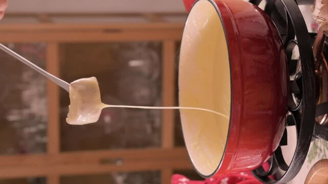 Cozy Swiss fondue setup with melted cheese, bread, pickles, and wine on a rustic table. advertising, social media campaigns, or food-related promotions. High quality 4k footage