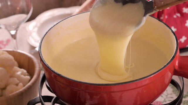 Cozy Swiss fondue setup with melted cheese, bread, pickles, and wine on a rustic table. advertising, social media campaigns, or food-related promotions. High quality 4k footage