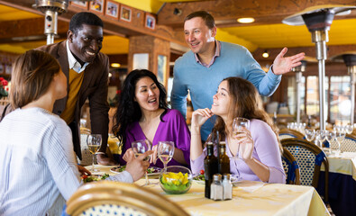 Smiling men invite women to dine for their table in the restaurant