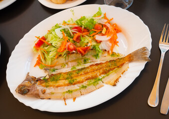 Fried baked whole solea fish are complemented with salad of fresh vegetable carrot, china cabbage, olives and decorated with tomato slice. Food styling, served lunch