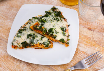 Restaurant serves portion of spinach pizza - triangular slices and glass of red wine. Pizza made according to traditional Italian recipe from fresh spinach leaves, large amount of young white cheese