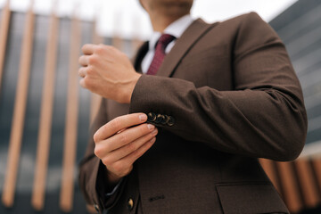 Close-up cropped shot of unrecognizable confident businessman adjusting suit button in city with modern architecture backdrop. Closeup low-angle view of business man adjusting suit outside.