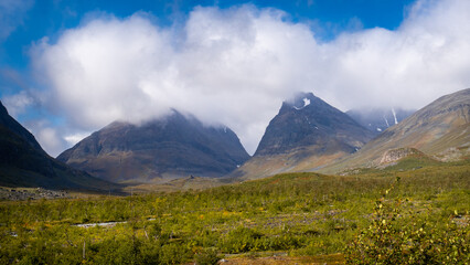 Fototapeta premium Breathtaking view to the Kebnekaise peak hidden in the clouds and scenic mountain valley shows beautiful swedish arctic nature in lapland during september when hiking to the arctic wilderness.
