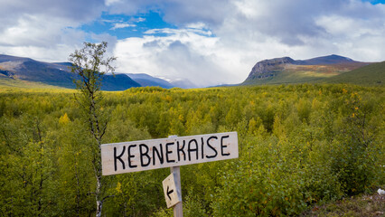 Panoramic view with Kebnekaise sign with arctic swedish lapland nature with tundra, birch forests, valley and mountains on horizon covered by clouds at the beginning of trail into swedish wilderness