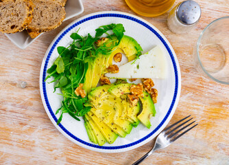 Avocado fruit is peeled and cut into slices on plate. Vegetarian snack complemented with cheese and walnut. View from above. Healthy, easily digestible snack, fruit food, energy source