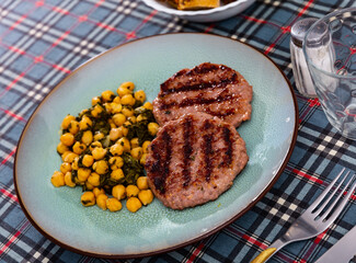 Flat cutlet cooked on electric grill and side dish made from vegetable products. Cutlet is complemented with stewed chickpeas and spinach.