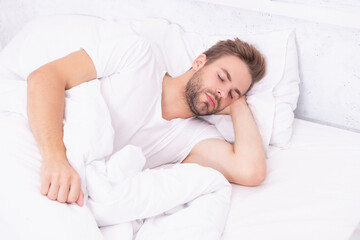 Sleepy man lying on bed sleeping at white bedroom. Asleep young man sleeping. Resting peacefully in comfortable bed. Lying with closed eyes. Deep male sleep. Man sleeping at night. Restful slumber