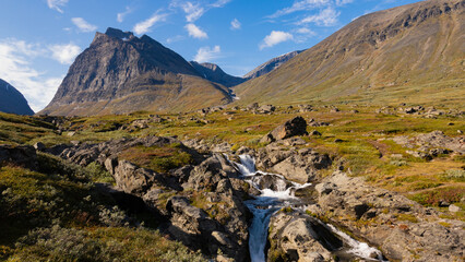 Under the Kebnekaise summit with mountains, dramatic peaks, valley, stream and swedish wilderness of nordic landscape during autumn beautiful day in Sweden while hiking and backpacking epic nature.