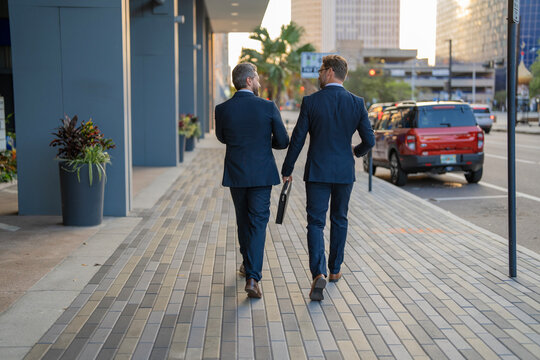 Two men businessmen colleagues or friends walking and talking in the street on the way to business office - Powered by Adobe