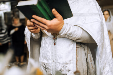 A Christian priest with a Bible in his hands, with a cross on his cassock, conducts a church service, prays in the church. Close-up photo, concept of religion.