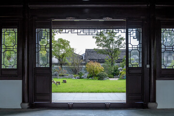 A symmetrical view from a pavilion through an ornately carved Chinese doorway with a traditional...
