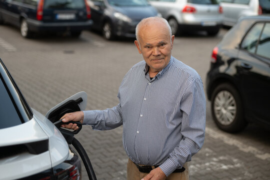 Senior Man Charging Electric Car with a Smile in Parking Lot