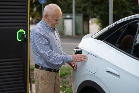 Senior Man Preparing to Charge Electric Car at Charging Station