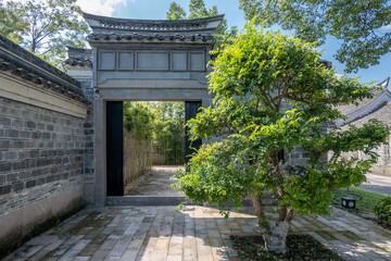 A traditional Chinese garden gateway or an ornate tiled roof entrance. The doorway leads to a stone-paved path with bamboo fencing of an oriental courtyard garden.