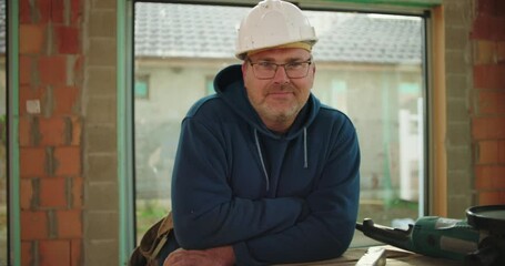Construction worker posing near workbench, wearing safety helmet in partially built structure, confident and approachable expression, construction site environment