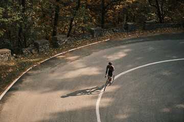 Cyclist rides a road bike on a scenic autumnal road. Sunlight illuminates the cyclist and the fall foliage. Perfect for travel, sports, and nature themes. Romania. Carpathian Mountains. Transylvania
