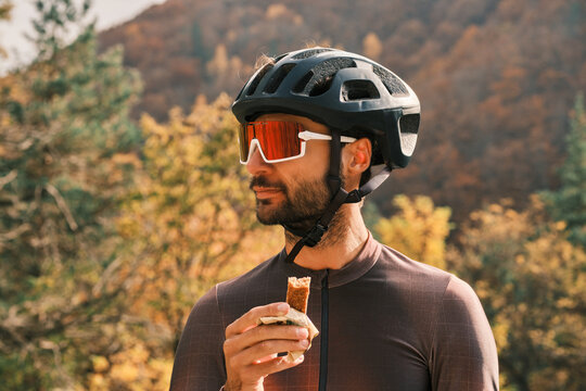 A cyclist enjoys a protein bar during a break in the autumn countryside.  He wears a helmet and cycling glasses. Perfect for active lifestyle, health and fitness themes.