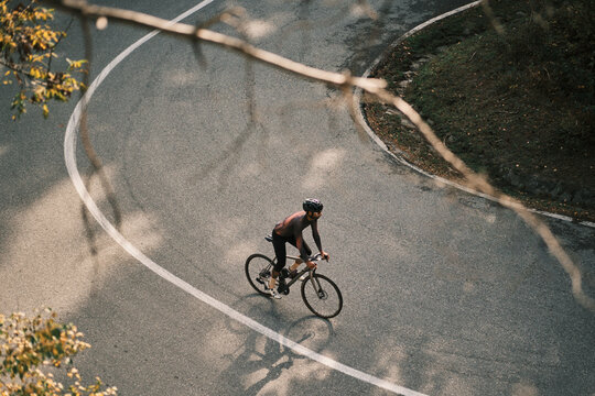 High-angle view of a cyclist riding a road bike on a winding road. Sunlight casts shadows on the asphalt.  Perfect for active lifestyle, sports, and travel themes.