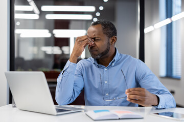 Stressed african american male businessman holds glasses, experiencing work frustration at laptop...