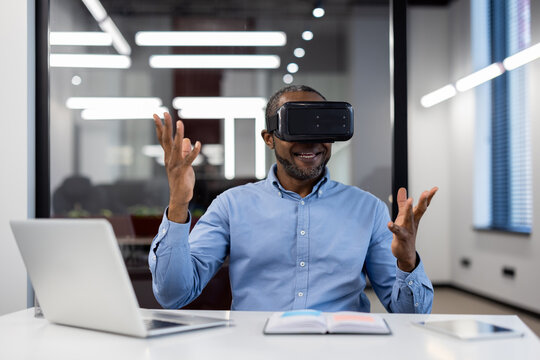 Mature african american businessman using virtual reality headset in office. Enthusiastically gesturing while exploring digital world. VR technology enhancing business creativity and strategy.
