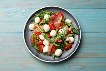 Tasty salad with arugula, mozzarella cheese, tomatoes and jamon on light blue wooden table, top view