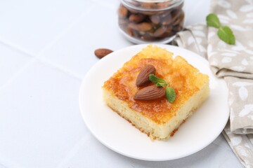 Slice of tasty semolina cake served on white tiled table, closeup. Space for text