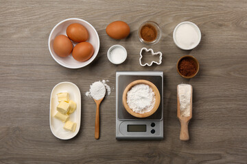 Kitchen scale with bowl of baking powder and other products on wooden table, flat lay