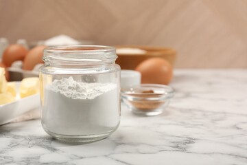 Baking powder in jar and other products on white marble table, closeup. Space for text