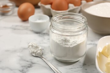Baking powder in jar and other products on white marble table, closeup