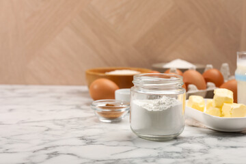 Baking powder in jar and other products on white marble table, closeup. Space for text
