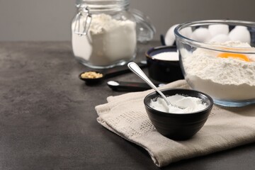 Baking powder and spoon in bowl on grey textured table, closeup. Space for text